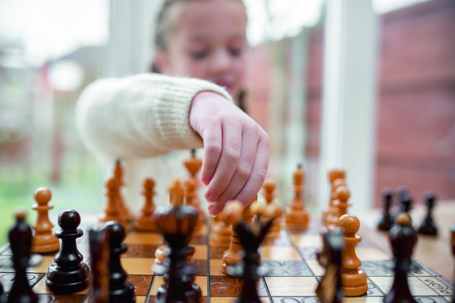 Beautiful cute genius child young girl playing chess game strategy with wooden pieces on chessboard kid concentrating planning move with king and queen